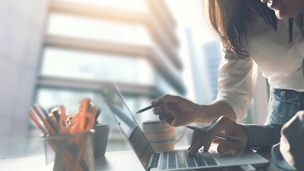 Deux collègues collaborant dans un bureau lumineux, discutant d'un projet sur un ordinateur portable, illustrant l'importance de l'engagement collectif et de la sensibilisation aux pratiques éco-responsables en milieu de travail.